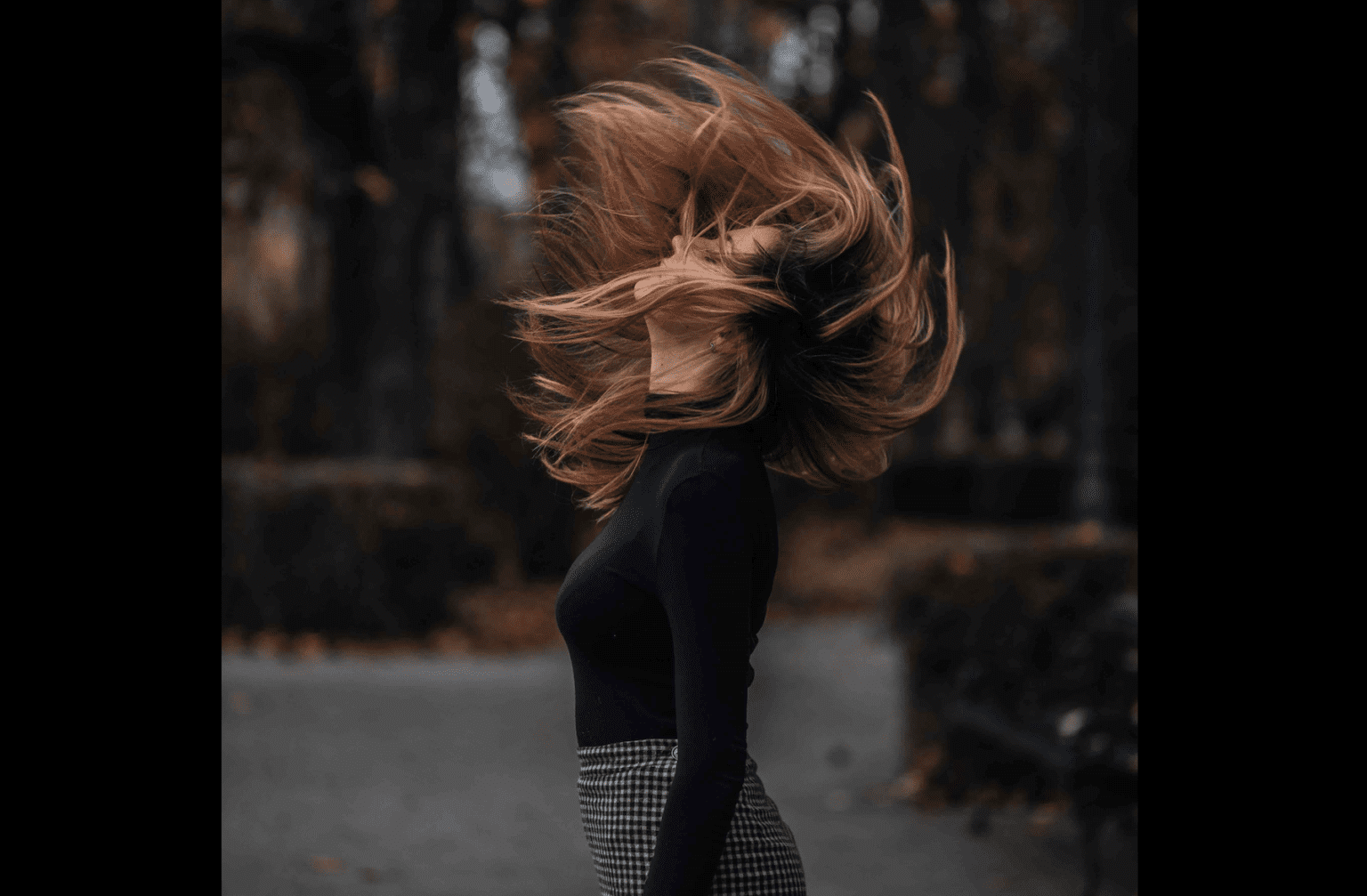 A stylishly attired girl in natural outdoor space flipping her hair from front to back. Hair Color Trends