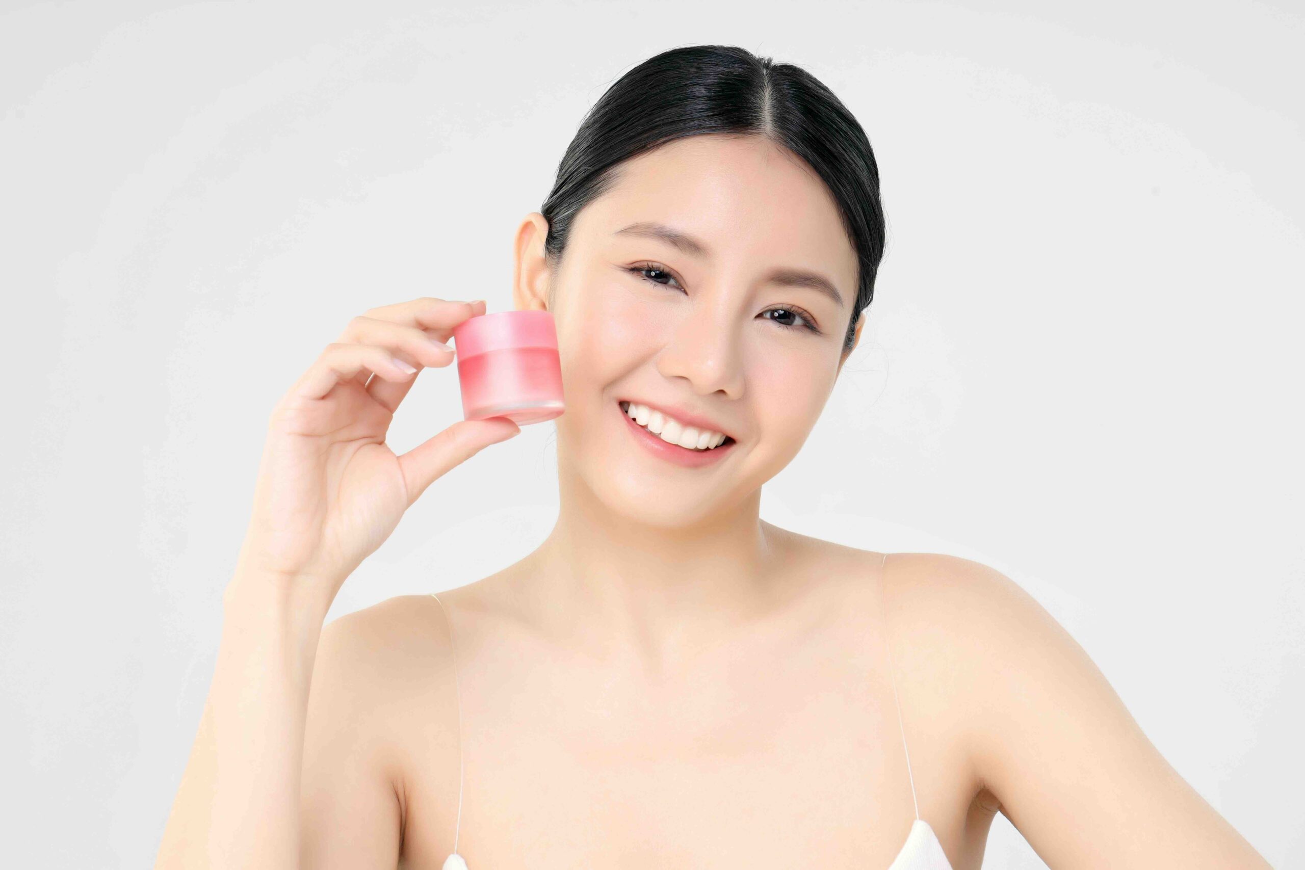 Close Up Beauty Face Asian Woman With Fresh Clean Skin Holding Facial Cream Bottle showing her routine of Korean Skincare. Standing on an Isolated on white background.