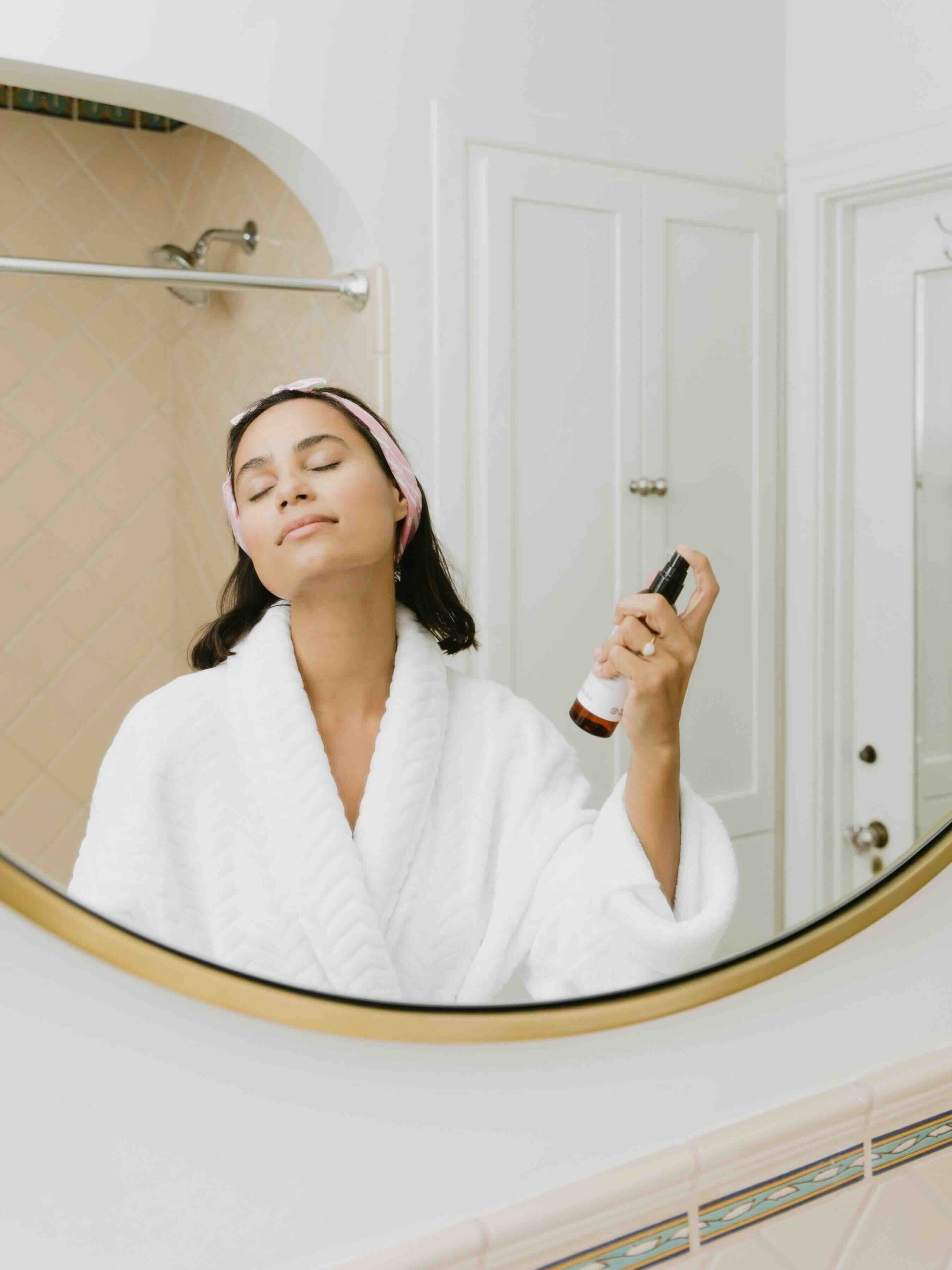 A woman in bathrobe spraying mist on her face as a part of her skincare routine
